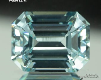 May include: A faceted, light blue Yttrium Aluminum Garnet gemstone. The emerald cut stone measures 9x7mm and weighs 3.57 carats. The image includes the text "Yttrium Aluminum Garnet", "Size 9x7mm", and "Weight 3.57 ct". The Gemtasy logo is visible.