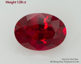 May include: An oval-cut, deep red ruby gemstone. The image includes text that reads "Grown Ruby Pigeon Blood, Size 7x5mm, Weight 1.08 ct." Additional text at the bottom reads "Any Cut, Any Size, We Bring Your Fantasies to Life!" and the brand name "GEMTASY."
