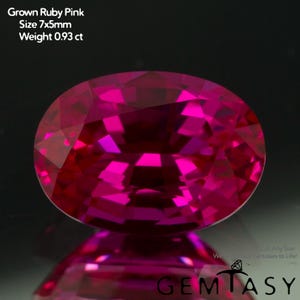 May include: A vibrant, oval-cut, grown ruby pink gemstone. The gem is 7x5mm and weighs 0.93 ct. The image includes the text "Grown Ruby Pink", "Size 7x5mm", and "Weight 0.93 ct". The gem is set against a dark background.