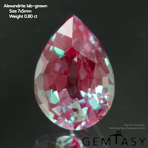 Può includere: Una gemma di alessandrite coltivata in laboratorio a forma di pera. La gemma è di colore rosso intenso con riflessi verdi e blu. La pietra misura 7x5mm e pesa 0,80 ct. L'immagine include anche il testo "Any Cut, Any Size We Bring Your Fantasies to Life!" e il nome del marchio "GEMTASY".