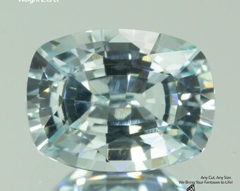 May include: A faceted, light blue Yttrium Aluminum Garnet gemstone. The cushion-cut stone is 8x6mm and weighs 2.13 carats. Text on the image reads "Any Cut, Any Size, We Bring Your Fantasies to Life!" and "GEMTASY".