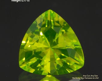 May include: A triangular, faceted, light green Lutetium Aluminum Garnet gemstone. The gem is 5x5x5mm and weighs 0.77 ct. Text on the image reads "Lutetium Aluminum Garnet, Size 5x5x5mm, Weight 0.77 ct" and "Any Cut. Any Size. We Bring Your Fantasies to Life!" with the logo "GEMTASY".