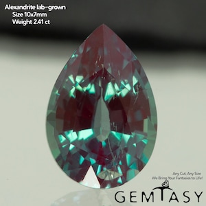 Può includere: Una gemma di alessandrite coltivata in laboratorio a forma di pera. La gemma è un mix di tonalità viola intenso e verde acqua. La dimensione è di 10x7mm e pesa 2,41 ct. L'immagine include anche il testo "Any Cut, Any Size We Bring Your Fantasies to Life!" e il marchio "GEMTASY".