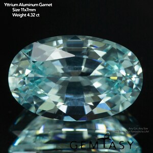 May include: An oval-cut Yttrium Aluminum Garnet gemstone, measuring 11x7mm and weighing 4.32 ct. The gem is a light blue colour with many facets, reflecting light. The text on the image reads "Yttrium Aluminum Garnet" and "GEMTASY".