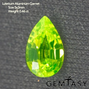 May include: A pear-shaped, bright lime green Lutetium Aluminum Garnet gemstone. The gem is 5x3mm and weighs 0.46 ct. The image also includes the text "GEMTASY".