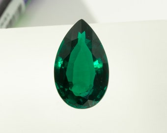 May include: A faceted, emerald-green gemstone in a teardrop shape. The gem has a polished surface with multiple facets that reflect light. The gemstone is set against a white background, highlighting its vibrant color and clarity. The gem is a vibrant green color.