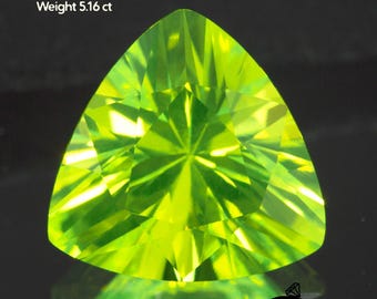 May include: A vibrant, triangular-cut, light green Lutetium Aluminum Garnet gemstone. The gem is 9x9x9mm and weighs 5.16 ct. The faceted surface reflects light, creating a brilliant display. The gemstone is set against a dark background.