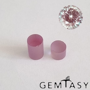 Può includere: Due piccole gemme cilindriche viola chiaro e una gemma rotonda sfaccettata sono esposte su sfondo bianco. Le gemme sono disposte vicino alla parte inferiore dell'immagine, con il logo "GEMTASY" sottostante.