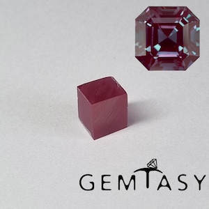 Può includere: Un cubo di pietra preziosa grezza color bordeaux accanto a una gemma sfaccettata a taglio quadrato. La gemma sfaccettata ha una tonalità bordeaux intenso con sfumature di viola e blu. L'immagine include anche il logo Gemtasy.