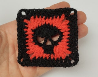 May include: Black crochet square with a red skull design.
