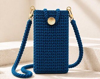 May include: A deep blue crochet crossbody phone bag featuring a textured stitch pattern, a matching braided shoulder strap, and a gold-toned circular button closure. The bag is rectangular in shape with gold metal swivel clasps on each side.