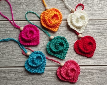 May include: Seven crocheted heart-shaped ornaments in various colors, including red, pink, blue, green, white, and orange. Each ornament has a wooden bead attached to a string.