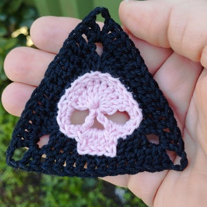 May include: A black crocheted triangle with a pink crocheted skull in the center.