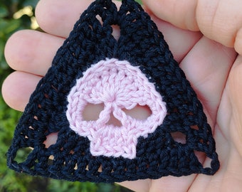 May include: A black crocheted triangle with a pink crocheted skull in the center.