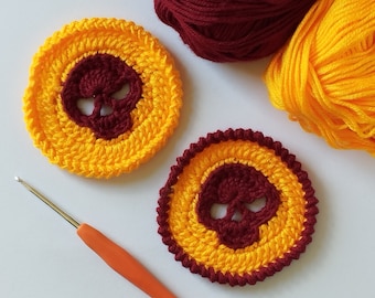 May include: Two crocheted skull coasters in yellow and maroon. The coasters are round and have a skull design in the center. The skull is crocheted in maroon and the background is crocheted in yellow.