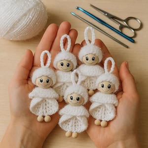 May include: Six handmade white angel ornaments with wooden heads and knitted bodies are held in a person's hands. Each angel has a loop for hanging. A ball of white yarn, a crochet hook, a needle, and scissors are in the background.