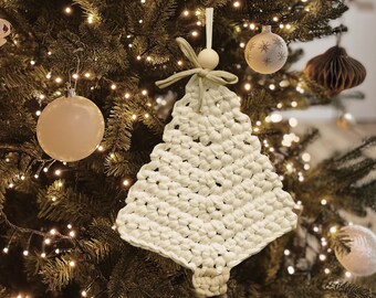 Op de afbeelding: Een witte gehaakte kerstboomversiering die aan een kerstboom met lichtjes hangt. De versiering is gemaakt van garen en heeft een rustieke, handgemaakte uitstraling.