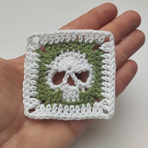 Peut inclure: Un carré de crochet blanc avec une bordure verte représentant un crâne blanc.
