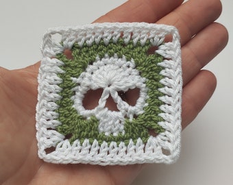 May include: A white crochet square with a green border featuring a white skull design.