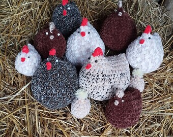 May include: A collection of handmade crocheted chicken toys in various colors and patterns, including brown, black, white, and beige. The toys are arranged on a bed of straw.