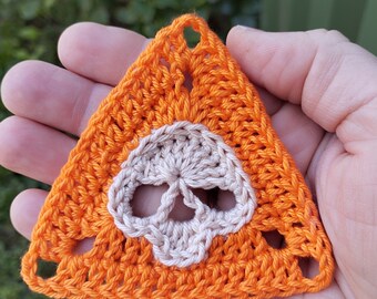 May include: Orange crocheted triangle with a white crocheted skull design in the center.