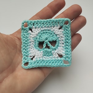 May include: A crocheted square with a white and turquoise skull design.