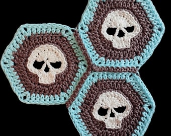 May include: Three crocheted hexagons with a skull design in white yarn on a brown and blue background.