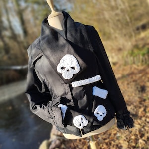 May include: A black jacket with a black scarf and white crocheted skull embellishments.