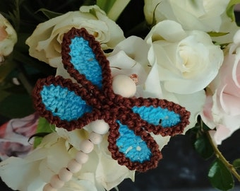 May include: A handmade crochet dragonfly with brown wings and blue accents, resting on white roses. The dragonfly has a wooden bead body and a small copper wire detail. The wings are a detailed crochet pattern.