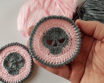 May include: Two crocheted skull appliques with a pink and gray color scheme. The skull is gray with a pink background and a gray border.