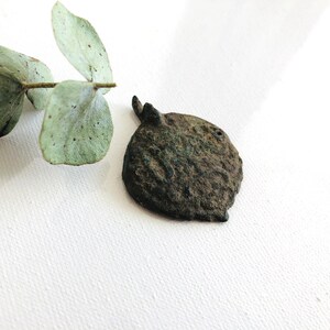 May include: A dark brown, round, metal pendant with a loop at the top. The pendant has a textured surface and appears to be antique.