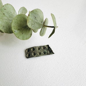 May include: A vintage metal pill box with 10 compartments. The pill box is brown and has a worn, rustic look. It is sitting on a white surface.
