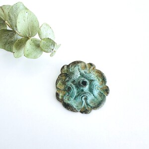 May include: A decorative metal rosette with a teal green patina and a small hole in the center. The rosette has a floral design with intricate details.
