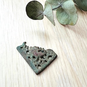 May include: A bronze-colored metal pendant with an intricate design. The pendant is shaped like a heart and has a cutout design that resembles a floral pattern.
