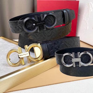 Puede incluir: Tres cinturones de cuero negro con hebillas decorativas. Uno tiene una hebilla dorada, otro una hebilla plateada y el tercero una hebilla negra. Los cinturones están colocados sobre una superficie clara.