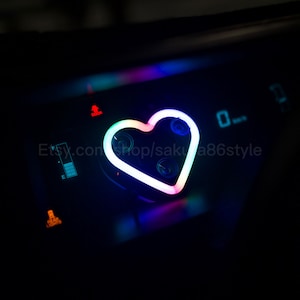 May include: A close-up of a car dashboard with a glowing heart-shaped light in the center. The light transitions through a spectrum of colors, with other illuminated symbols and text visible. The Etsy shop name is visible.