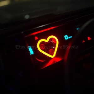 Pode incluir: Painel do carro iluminado com uma forma de coração amarelo brilhante e detalhes em vermelho. O painel também apresenta luzes indicadoras azuis e vermelhas. O nome da loja Etsy é visível.