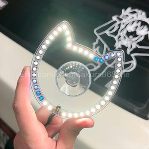 May include: A white cat-shaped LED light with a suction cup on the back. The light is on and illuminating the surrounding area.