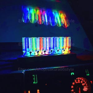 May include: A set of eight colorful LED lights, each with a cylindrical shape and a grid pattern. The lights are arranged in two rows, with four lights in each row. The lights are illuminated in a variety of colors, including red, green, blue, and purple. The lights are mounted on a black base. Etsy.com/shop/sakura86style