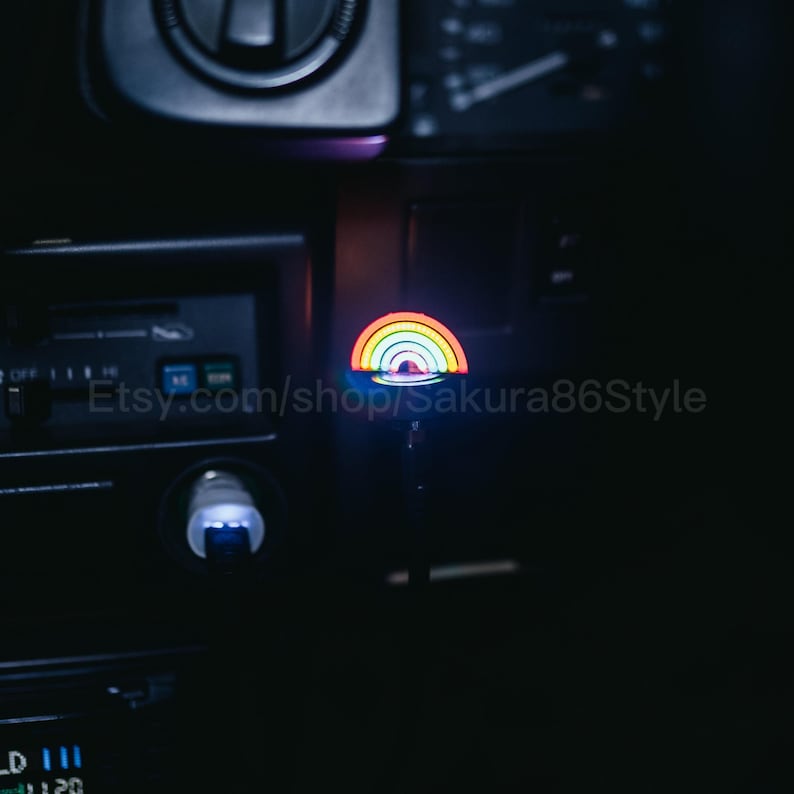 May include: A multi-coloured rainbow LED light, with red, orange, yellow, green, and blue arcs, illuminates the interior of a car. The Etsy shop name "sakura86Style" is visible. The light is mounted on a black surface.