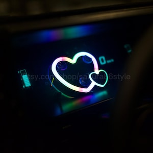 May include: A car dashboard with a glowing heart-shaped design in neon colors. The design is composed of two hearts, one larger than the other. The dashboard also displays a fuel gauge and a speed indicator showing 0 mph.