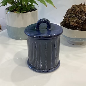 May include: A blue ceramic jar with a lid and a handle. The jar has a textured surface with vertical lines.