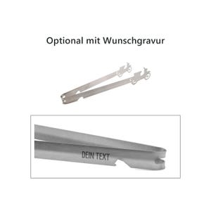 Op de afbeelding: Een zilverkleurige metalen tang met een uitgesneden ontwerp van een oldtimer aan de uiteinden. De tekst "Optional mit Wunschgravur" staat erboven en een close-up toont de tekst "DEIN TEXT" gegraveerd op het metalen oppervlak.