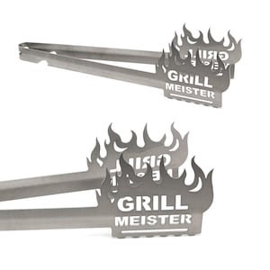 Peut inclure: Pinces de cuisine en acier inoxydable avec un motif de flammes et les mots "GRILL MEISTER" découpés. Les pinces sont présentées sur un fond blanc.