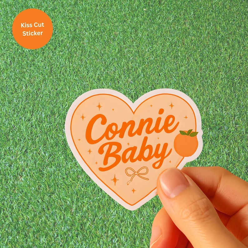 May include: A heart-shaped sticker with the words "Connie Baby" in orange script. The sticker has a peach illustration and a small bow. An orange circle sticker in the upper left corner reads "Kiss Cut Sticker".