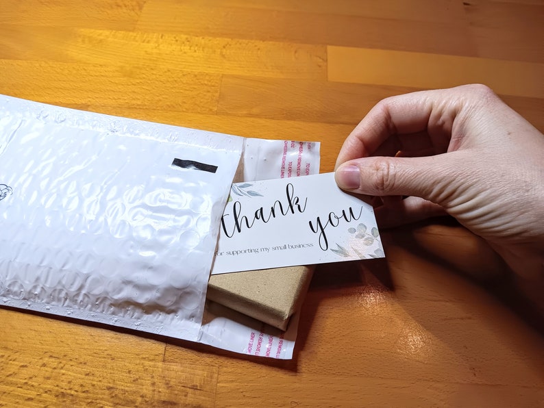 May include: A white padded envelope with a small brown box inside. A white card with the text "thank you for supporting my small business" is being pulled out of the envelope.