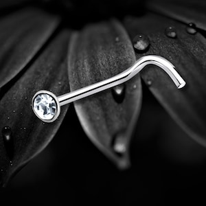 May include: A silver nose ring with a clear crystal gemstone. The ring is curved and has a small ball at the end.