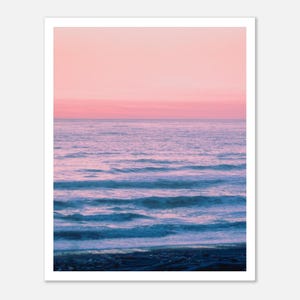 Könnte beinhalten: Ein rosa und blauer Sonnenuntergang über einem ruhigen Meer mit sanft rollenden Wellen, die auf das Ufer zulaufen.