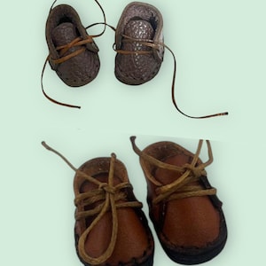 May include: Two pairs of dark brown leather shoes with brown laces. The shoes are tied with a bow. The shoes are small and appear to be for a doll or a child.
