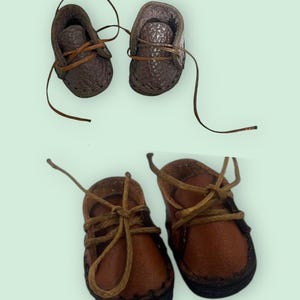 May include: Two pairs of miniature shoes. The top pair is dark brown textured leather with thin laces. The bottom pair is smooth medium brown leather with thicker tan laces. The text "DARK BROWN LEATHER SHOES" is visible at the top of the image.